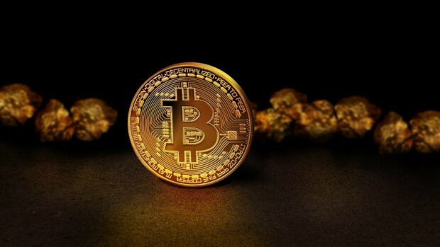 A golden Bitcoin coin with intricate digital circuits stands on a dark surface with blurred golden nuggets behind, HD Desktop Wallpaper