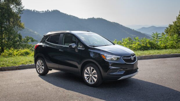 A black Buick Encore is parked on a roadside with green trees and mountains in the background, 2K Desktop Wallpaper