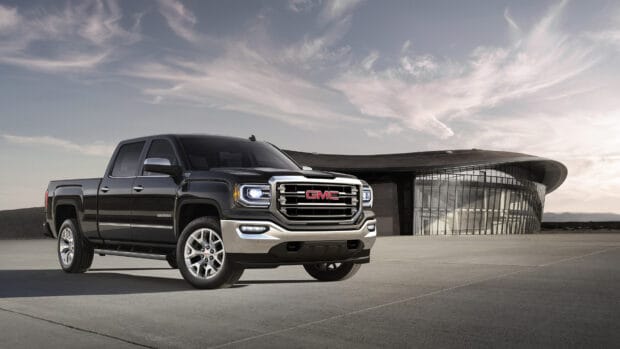 A black GMC Sierra is parked on a concrete surface in front of a modern curved glass building under a cloudy sky, 4K Desktop Wallpaper