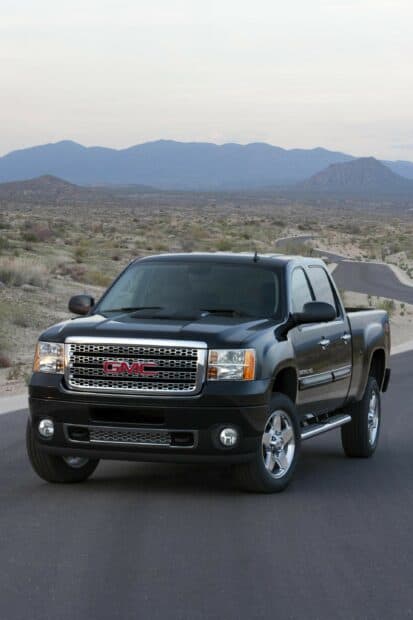 A black GMC Sierra is parked on a desert road with mountains in the background, 2K Phone Wallpaper