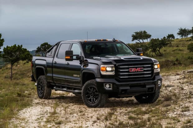 A black GMC Sierra is parked on a rocky terrain with trees and cloudy sky in the background, HD Desktop Wallpaper