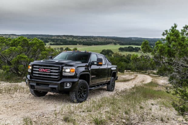 A black GMC Sierra truck is parked on a rugged dirt road surrounded by greenery and hills, HD Desktop Wallpaper