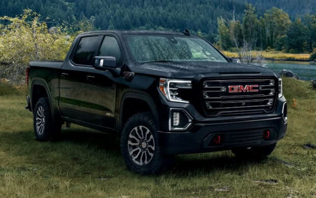 A black GMC Sierra truck is parked on grassy land near a lake with a forest background, HD Desktop Wallpaper