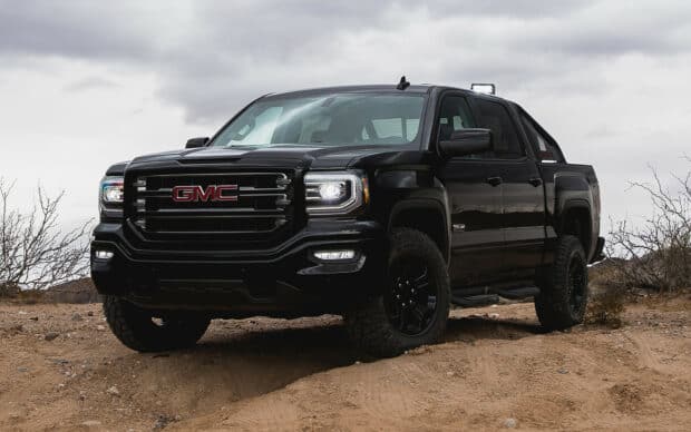 A black GMC Sierra truck is parked on rugged sandy terrain under a cloudy sky, HD Desktop Wallpaper