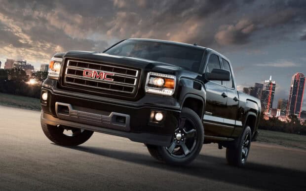 A black GMC Sierra truck is parked on a concrete surface with city buildings in the background, HD Desktop Wallpaper