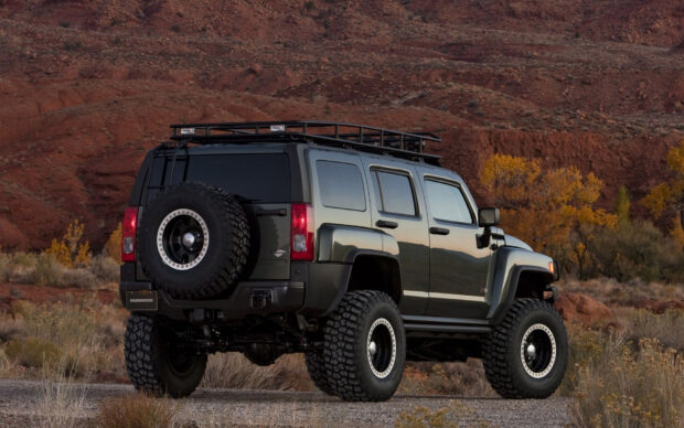 A black Hummer H3 is parked on rugged terrain with a rocky red cliff and autumn trees in the background, HD Desktop Wallpaper