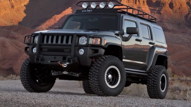 A black Hummer H3 is parked on rocky desert ground with mountain cliffs in the background, HD Desktop Wallpaper