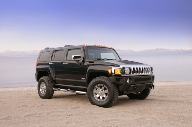 A black Hummer H3 is parked on a sandy shore with calm water and mountains in the background, HD Desktop Wallpaper