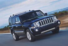 A black Jeep Commander is shown driving at high speed on a winding road with a scenic landscape in the background, 2K Desktop Wallpaper