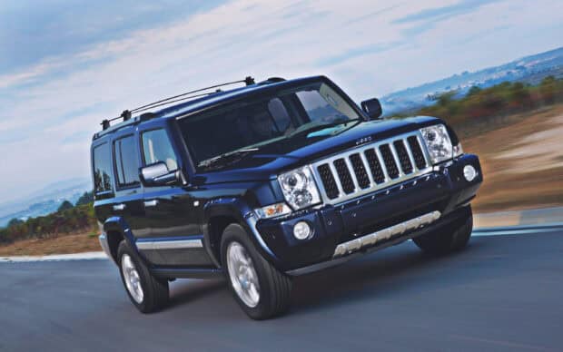 A black Jeep Commander is shown driving at high speed on a winding road with a scenic landscape in the background, 2K Desktop Wallpaper