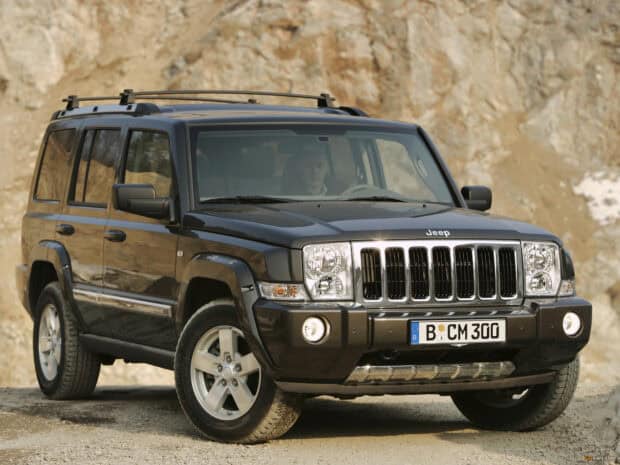 A black Jeep Commander is parked on a rough dirt surface with rocky cliffs in the background, HD Desktop Wallpaper