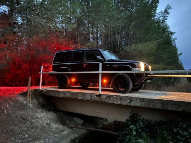 A black Jeep Commander is parked on a bridge surrounded by trees with red and yellow lights illuminating the scene, HD Desktop Wallpaper