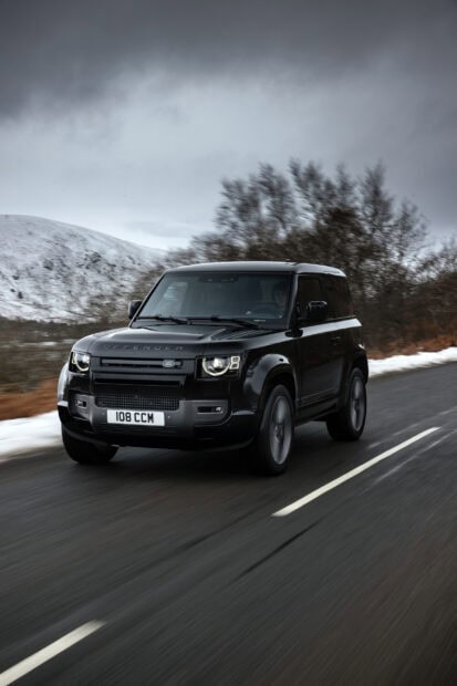 A black Land Rover Defender driving on a winding road near snowy hills and trees, 2K Mobile Wallpaper