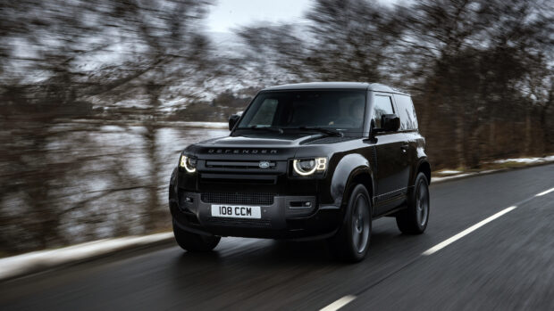 A black Land Rover Defender is driving quickly on a wet road with trees in the background, 4K Desktop Wallpaper