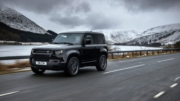 A black Land Rover Defender drives along a snowy mountain road under cloudy skies, 4K Desktop Wallpaper