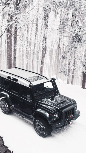 A black Land Rover Defender driving through a snowy forest landscape with frosted trees, 4K Mobile Wallpaper