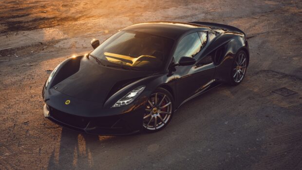 A black Lotus Emira sports car is parked on a rough surface in warm sunlight, HD Desktop Wallpaper