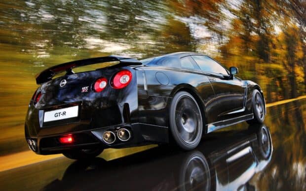 A black Nissan GT R driving fast with autumn trees reflected on its shiny surface, HD Desktop Wallpaper