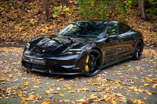 A black Porsche Taycan is parked on a leaf covered road in autumn, HD Desktop Wallpaper