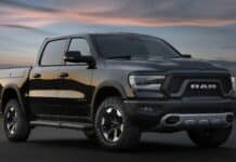 A black Ram pickup truck parked on a road during sunset with city lights in the background, 2K Desktop Wallpaper