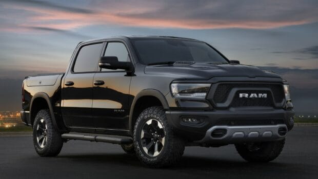 A black Ram pickup truck parked on a road during sunset with city lights in the background, 2K Desktop Wallpaper