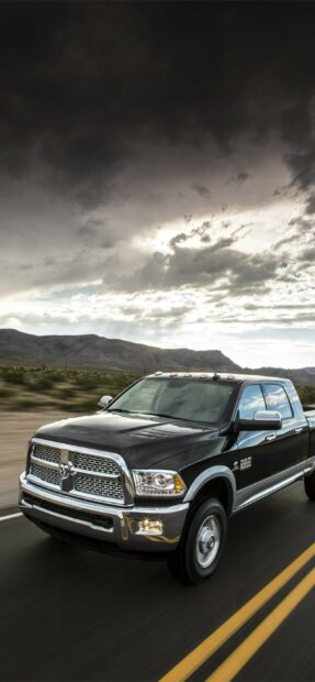 A black Ram pickup is driving on a road with mountains and dramatic clouds in the background, 2K Mobile Wallpaper