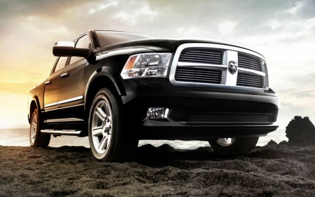 A black Ram pickup truck is parked on a sandy shore with the ocean and a cloudy sky in the background, HD Desktop Wallpaper
