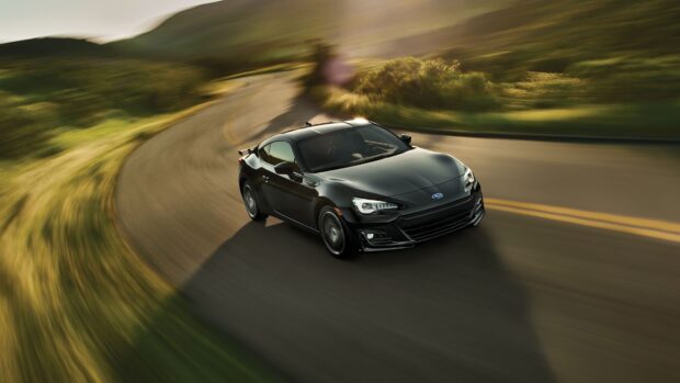 A black Subaru BRZ is seen driving swiftly along a winding road with blurred background motion, 4K Desktop Wallpaper