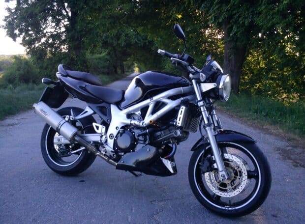 Black Suzuki Sv650 motorcycle is parked on a quiet rural road surrounded by trees and greenery, 2K Desktop Wallpaper