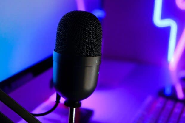 A black studio microphone stands on a desk with colorful neon lights behind it, 2K Desktop Wallpaper