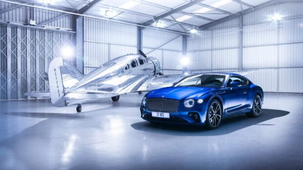 A blue Bentley Continental GT is parked in a bright hangar next to a vintage silver airplane, 2K Desktop Wallpaper