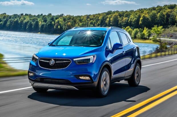 A blue Buick Encore drives along a road beside a lake with green trees in the background, HD Desktop Wallpaper