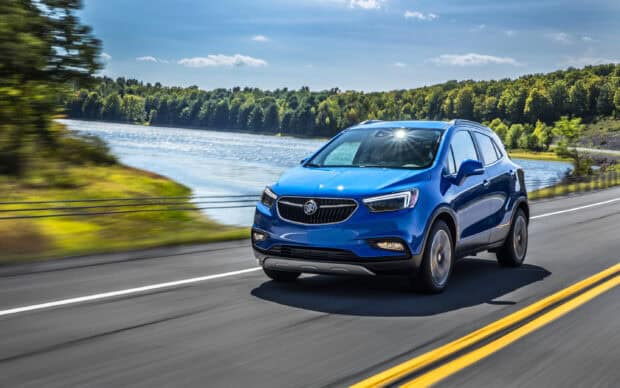 A blue Buick Encore drives along a lakeside road surrounded by trees and clear skies, 2K Desktop Wallpaper