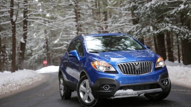 A blue Buick Encore driving through a snow covered forest road with headlights on, 4K Desktop Wallpaper