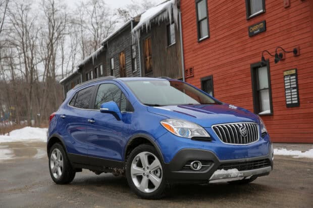 A blue Buick Encore is parked near wooden buildings with icicles hanging above on a winter day, 2K Desktop Wallpaper
