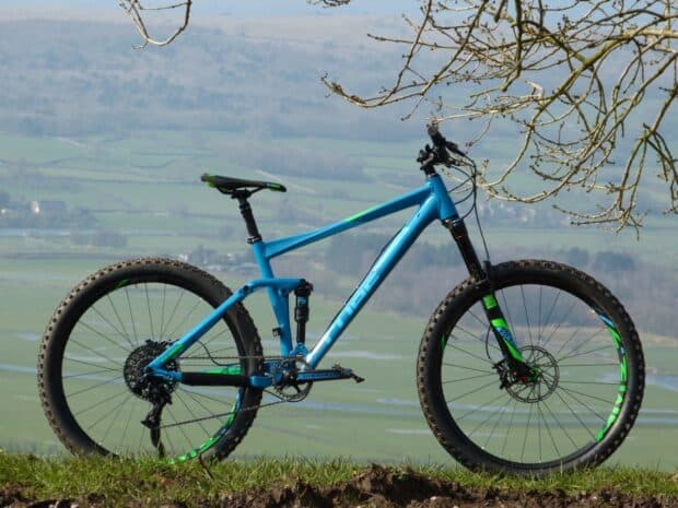 A blue Cube bike stands on a grassy hill with a scenic valley in the background, HD Desktop Wallpaper