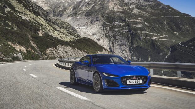 A blue Jaguar F Type is driving along a curved mountain road with rocky cliffs in the background, 2K Desktop Wallpaper