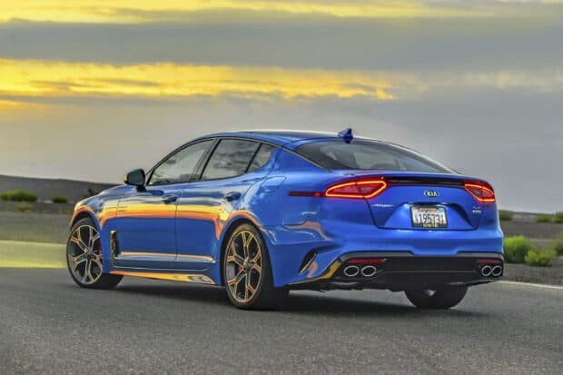 A blue Kia Stinger is parked on an open road with a dramatic yellow sunset sky, 2K Desktop Wallpaper