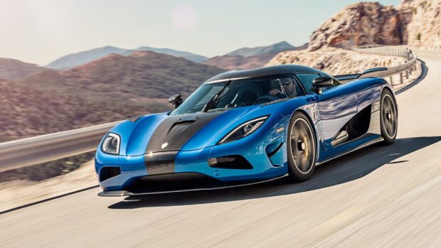 A blue Koenigsegg is driving fast with scenic mountains in the background, 2K Desktop Wallpaper