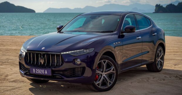 A blue Maserati Levante is parked on a sandy beach with sea and islands in the background, 2K Desktop Wallpaper