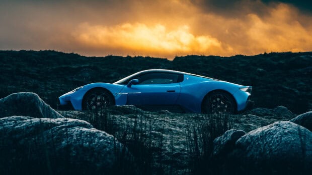 The blue Maserati MC20 stands on rocky ground with a dramatic sunset sky in the background, 2K Desktop Wallpaper