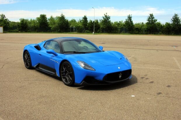 A blue Maserati MC20 is parked on an open tarmac with trees in the background, 2K Desktop Wallpaper
