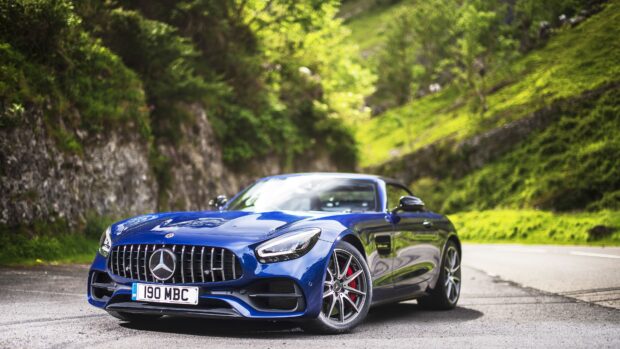 A blue Mercedes Benz AMG GT is parked on a winding mountain road surrounded by greenery, 4K Desktop Wallpaper
