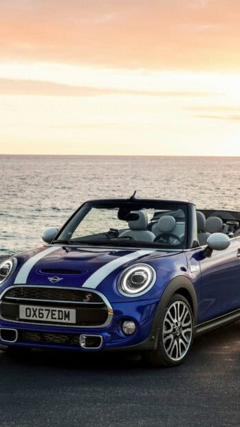A blue Mini Cooper convertible is parked near the ocean during sunset showing its front view, HD Phone Wallpaper
