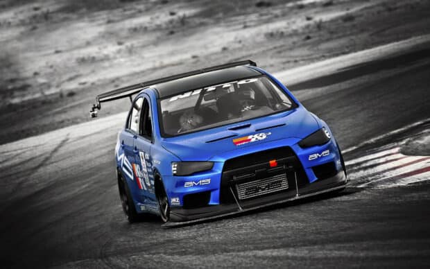 A blue Lancer Evo is seen speeding on a racetrack with a driver inside, HD Desktop Wallpaper