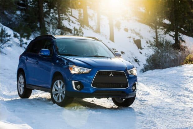 A blue Mitsubishi Outlander drives through a sunny snowy forest road, HD Desktop Wallpaper