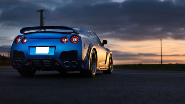 A blue Nissan GT R is parked on an empty road under a colorful sunset sky, 4K Desktop Wallpaper