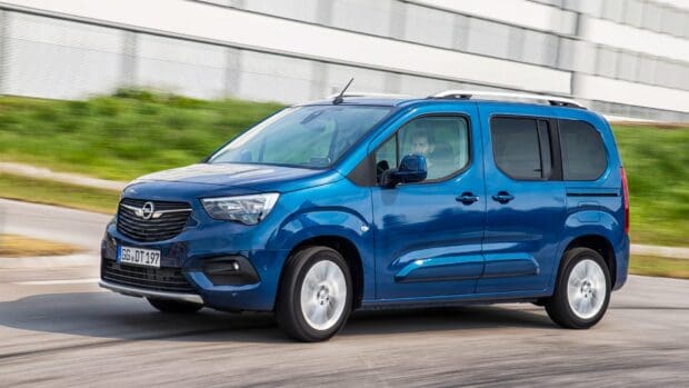 A blue Opel Combo driving past a green grassy area with a modern building in the background, HD Desktop Wallpaper