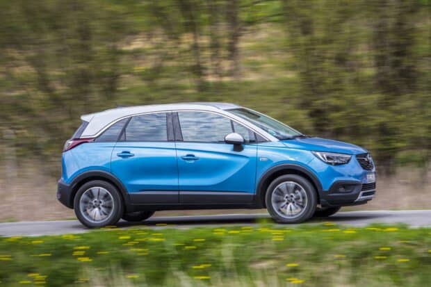 A blue Opel Crossland is captured driving swiftly through a green countryside road, HD Desktop Wallpaper