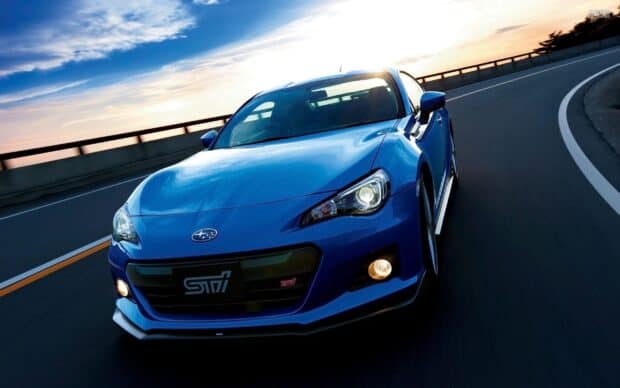 A blue Subaru Brz is shown driving on a curved highway during sunset, 2K Desktop Wallpaper